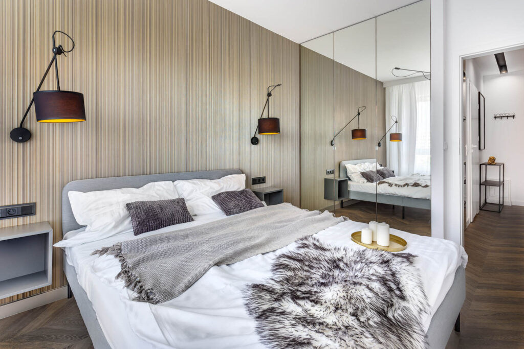 "Wnętrze tego pokoju zachwyca swoją spójnością i ciepłem. Podłoga wykonana jest z jednolitego materiału, który przechodzi z przedpokoju do pomieszczenia, tworząc jednolity klimat. Na ścianie zastosowano tapetę 3D, która nadaje pomieszczeniu głębi i wyjątkowego charakteru. Kolory dobrano ze szczególną starannością - ciepłe odcienie brązu i beżu tworzą przyjemną i harmonijną atmosferę. Wszystko to sprawia, że wnętrze wydaje się przytulne i zapraszające, idealne do relaksu po długim dniu."